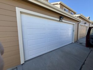 A white double garage door is closed on a tan house with cream trim. A number 