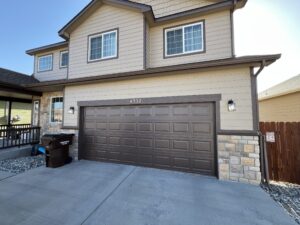 Two-story beige house with brown trim, stone accents, and a double garage door with the number 4537 above it. Trash bins and outdoor lights are by the garage.
