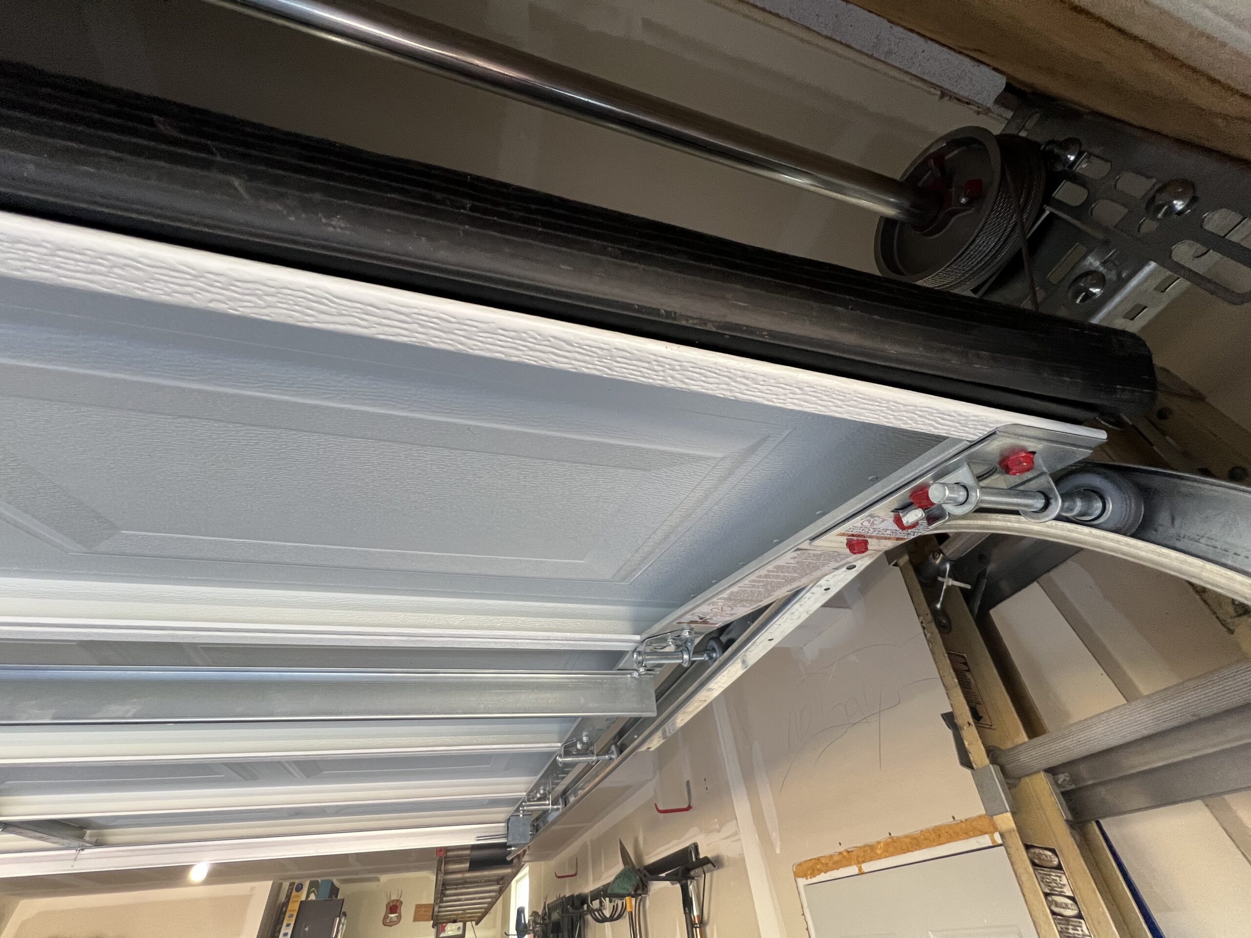Close-up view of a garage door from the inside, showing metal tracks, a torsion spring, and part of the automatic opener mechanism.